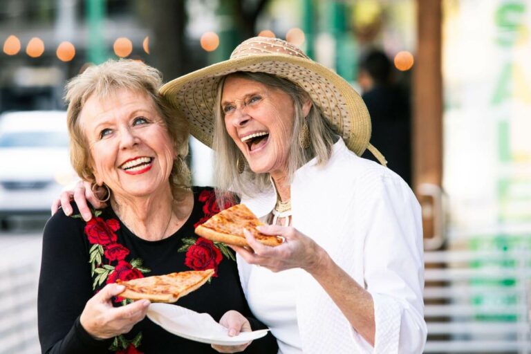 Two women embracing and smiling while holding slices of pizza