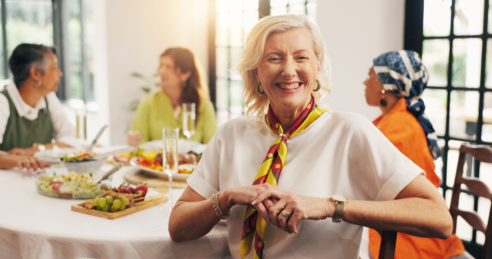 What Is the Best Age to Move Into Senior Living Smiling senior woman sitting at the dinner table with friends